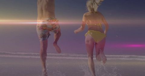 Couple running into surf at sunset jumping and splashing on tropical beach summer joy