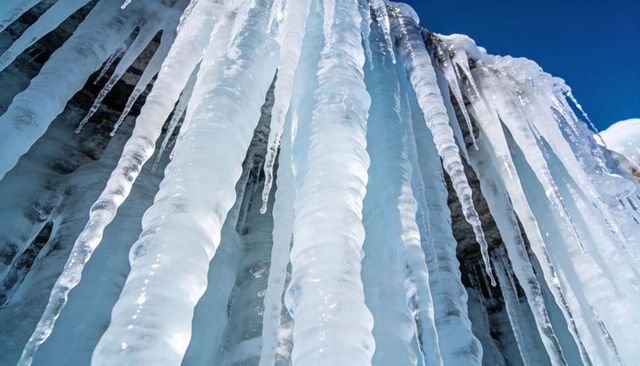 Glinting icicles dripping from rocky ledge under vivid blue sky