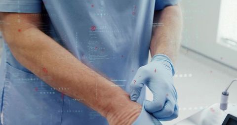 Male healthcare worker putting on gloves in clinical room with digital data overlay