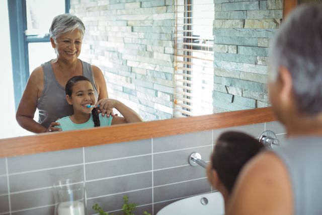 Grandmother and granddaughter brushing teeth together in a modern bathroom, reflecting family bonding and morning routine. Ideal for use in articles about family life, dental hygiene, intergenerational relationships, and healthy habits.