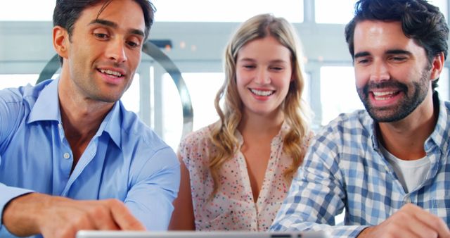 Team members are collaborating and smiling while working on a digital project in a modern office environment. Suitable for use in presentations, business websites, blog posts about teamwork, corporate training materials, and promotional materials emphasizing teamwork and cooperation in the workplace.