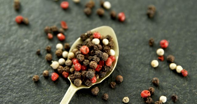 Close-up view of mixed peppercorns including black, white, and pink varieties, scattered around and on a silver spoon. Perfect for cooking blogs, recipes, culinary product packaging, and spice-related articles.