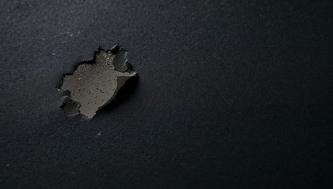 Peeling black coating revealing brown primer with curled edges and water droplets