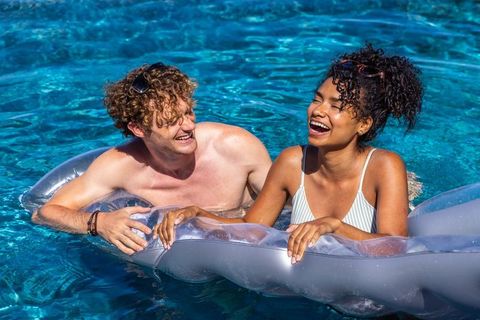 Laughing diverse couple floating on clear inflatable in bright blue pool