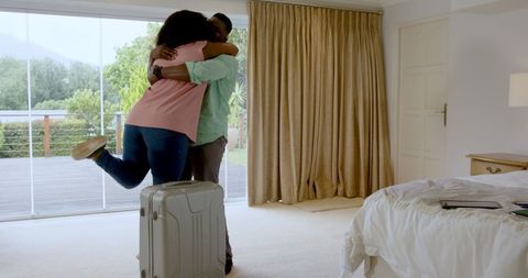 Joyful Reunion of Couple Embracing in Sunlit Bedroom with Luggage