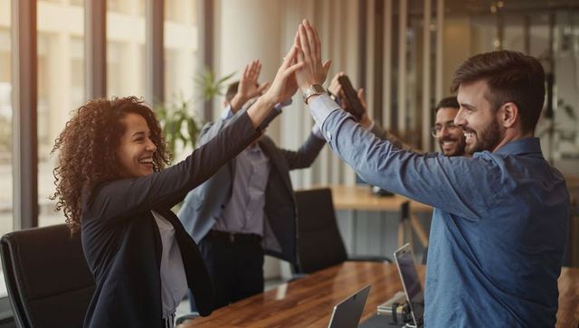 Team high-five in modern boardroom celebrating project success and collaborative win