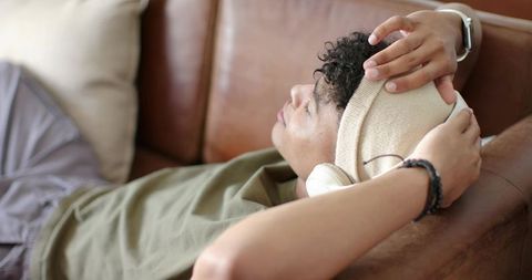 African american man relaxing on leather sofa wearing headphones companion adjusting beanie