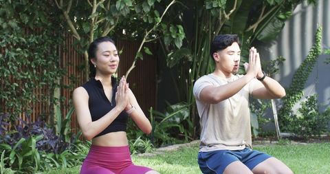 Asian couple meditating on garden lawn wearing sportswear and smartwatches for wellness