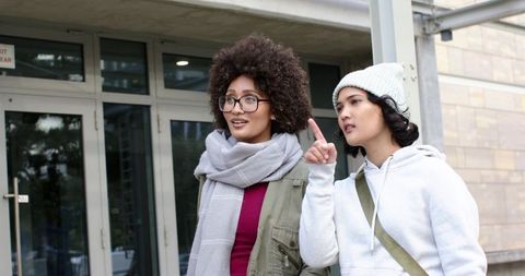 Two friends exploring campus entrance pointing direction, casual urban winter outfits