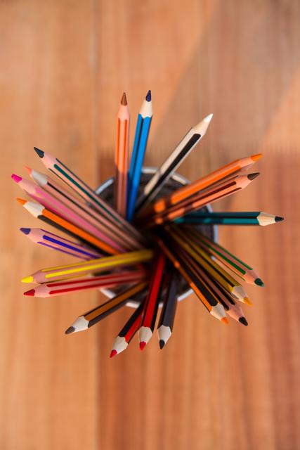 Color pencils arranged in a holder viewed from above on a wooden surface. Ideal for educational materials, art and craft projects, school promotions, and office supply advertisements.