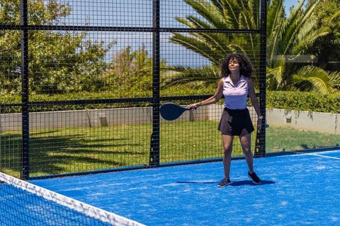 African american woman playing padel on vibrant blue court holding racket