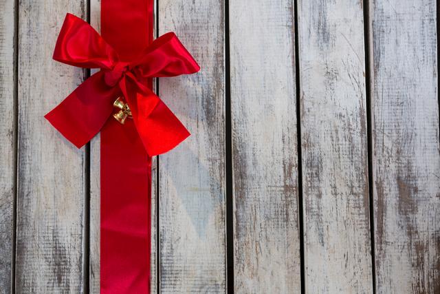 Red ribbon tied in a bow on a rustic wooden plank, perfect for holiday-themed designs, Christmas cards, festive invitations, and seasonal marketing materials.