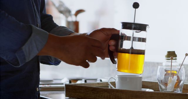 Man pouring freshly brewed coffee from French press into cup in modern kitchen. Perfect for themes of morning routines, breakfast, coffee lovers, and beverage preparation.