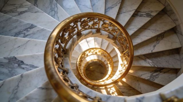 Spiral marble staircase with ornate gilded balustrade in luxurious grand hotel interior