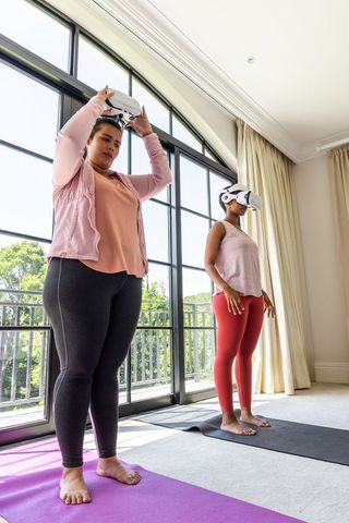 African american women practicing virtual reality yoga on balcony mats at home