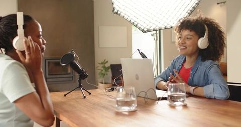 Diverse female co-hosts recording podcast at home studio with laptop and microphones