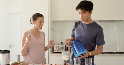 Asian man and caucasian woman preparing protein smoothie, adding supplement powder
