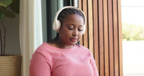 African american woman sitting by patio wearing white headphones listening with calm
