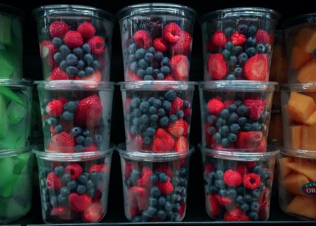 Various types of berries, including strawberries, blueberries, and raspberries, arranged in clear plastic containers stacked on a grocery store shelf. This image is perfect for marketing materials related to healthy eating, organic produce, grocery advertisements, and food blog posts. The vibrant colors and freshness of the fruits highlight the quality of the produce available.