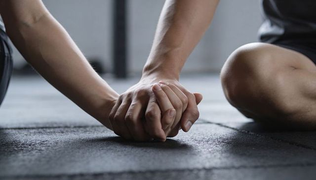 Athletes clasping hands on rubber gym floor showing teamwork support and recovery