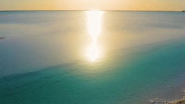 Golden sunrise reflecting over turquoise lagoon with vertical sun column