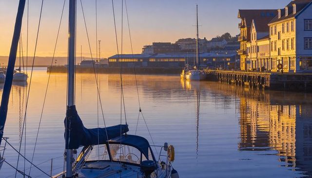 Golden hour sailboat docked in calm coastal marina with pier and building reflections