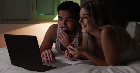 Happy Couple Relaxing in Bedroom Watching Laptop