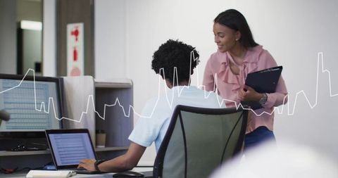 Coworkers collaborating at desk reviewing laptop analytics with line graph overlay