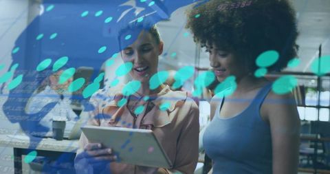 Two women collaborating over tablet in modern coworking space with teal digital overlay