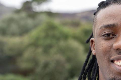 Half-face close-up of african american man smiling showing dreadlocks with greenery background