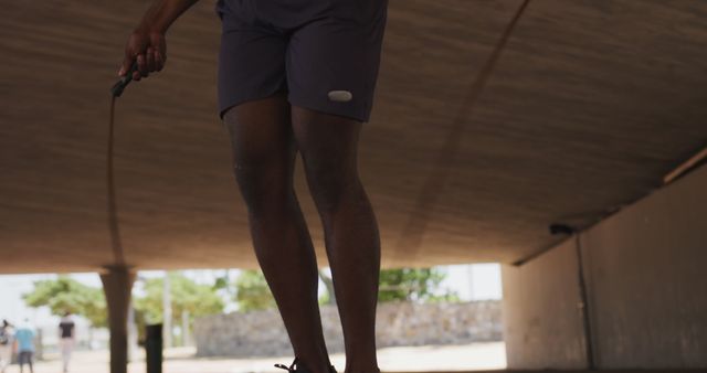 This close-up of a man jumping rope under an overpass in casual sportswear captures the essence of an active and healthy lifestyle. Ideal for use in fitness blogs, exercise guides, sportswear advertisements, or workout motivation posts.