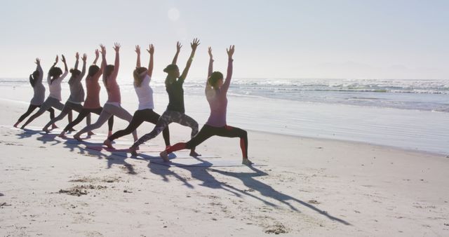 Group performing yoga poses on sandy beach with ocean view, highlighting fitness and wellness in outdoor setting. Perfect for promoting fitness retreats, yoga courses, or relaxation exercises at coastal venues.