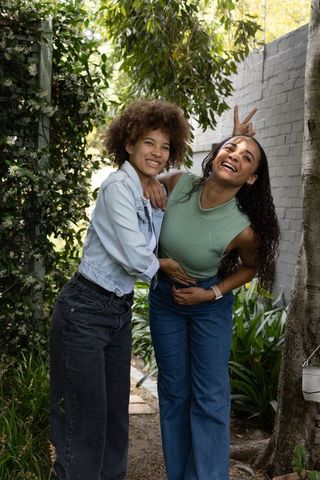 Laughing african american friends leaning together on garden path wearing denim and casual tops