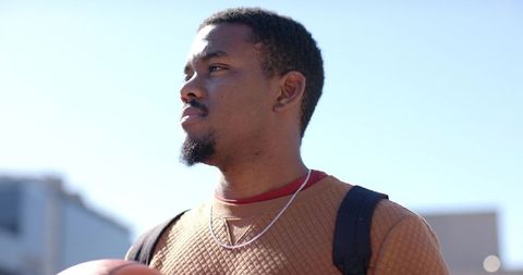 African american man holding basketball looking toward sky urban portrait backpack