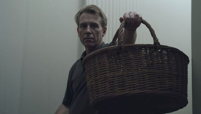 Serious middle-aged man holding wicker basket in narrow hallway presenting rustic hamper