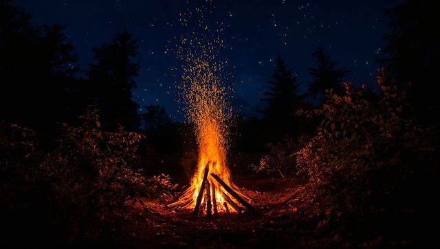Night bonfire blazing in forest clearing with sparks rising under starry sky