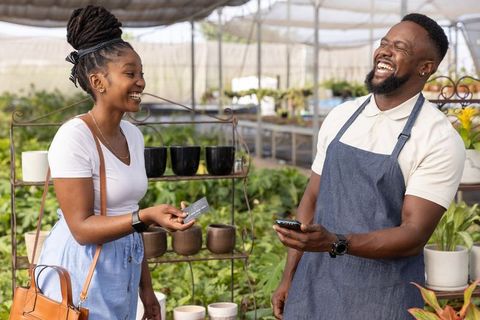 African american customer making contactless payment at plant nursery, staff laughing and chatting