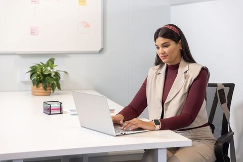 Mid-adult asian woman working at laptop in clean minimalist office focusing on productivity