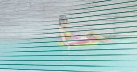 Relaxing woman floating on rainbow inflatable in turquoise pool with horizontal stripes