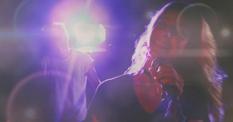 Lead singer holding microphone under pink stage lights with lens flares, live concert