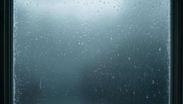 Rainy window with droplets and condensation blurring exterior for moody blue background
