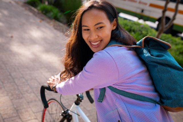 Smiling asian woman wearing backpack and riding bike in street - Download Free Stock Photos Pikwizard.com