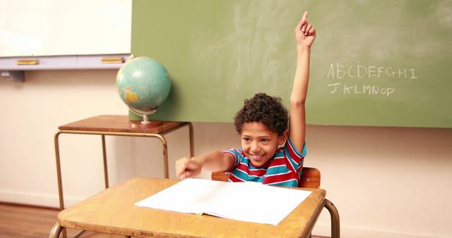 Young student raising hand while sitting at desk in classroom. Suitable for educational content, advertisements for school supplies, learning programs, or campaigns encouraging student engagement in learning.