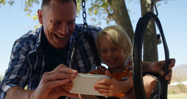 Father and Son Bonding on Swing Set, Smiling and Engaging with Tablet Device - Download Free Stock Images Pikwizard.com