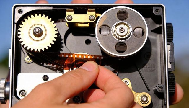 Hand threading 35mm film through vintage camera mechanism with exposed metal gears closeup