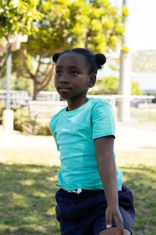African american girl standing in sunny park wearing turquoise t-shirt and two buns