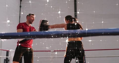 Female boxer training with coach holding focus mitts in boxing ring, dynamic sparring