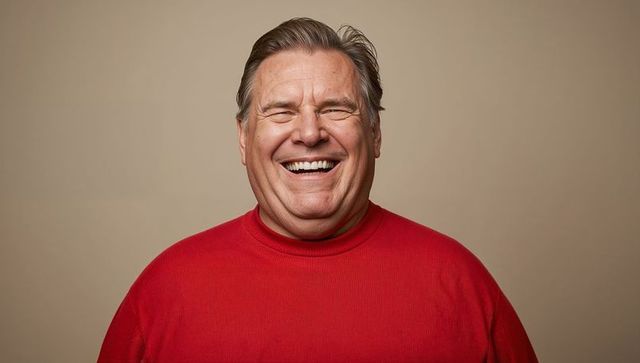 Laughing senior man wearing red crewneck sweater smiling with closed eyes joyful portrait
