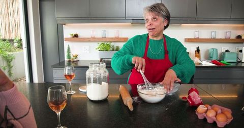 Cheerful mother baking and enjoying wine in modern kitchen