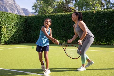 Mother and daughter playing tennis in sunny garden court